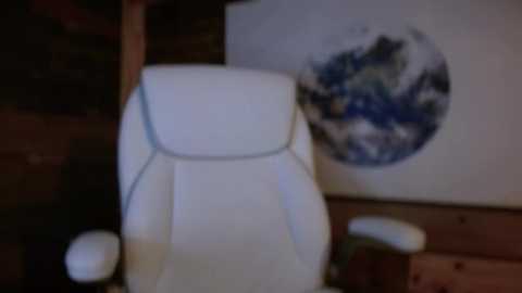 Media: A blurred video of a white leather office chair with armrests in the foreground. In the background, a framed, slightly out-of-focus globe map with blue and white colors is mounted on a wooden wall.