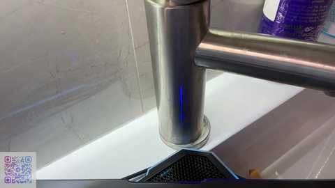 Media: Video of a sleek, modern stainless steel faucet with a blue LED light strip, mounted on a white countertop. The background features a marble tile backsplash.