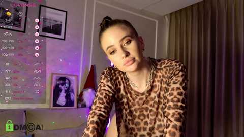 Media: Video of a young woman with light skin and a high ponytail, wearing a leopard print top, in a dimly lit room with a digital display showing streaming metrics.