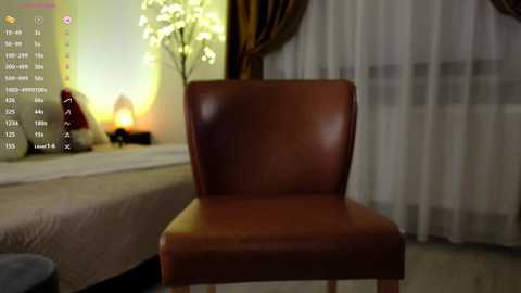 Media: A video of a brown leather chair in a dimly lit bedroom with white curtains, a bed, and a lamp emitting a warm glow.