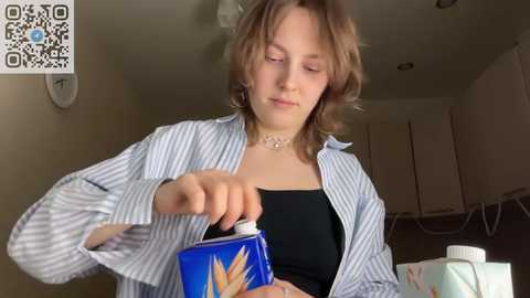 Media: A video of a young woman with light brown hair, wearing a striped shirt, pouring milk from a blue carton into a glass.