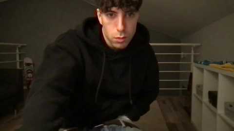 Media: A video of a young man with curly hair, wearing a black hoodie, leaning over a console game. The background shows a modern, dimly lit living room with white furniture and a bookshelf.