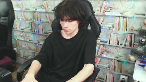 Media: Video of a young, fair-skinned, dark-haired boy in a black T-shirt, sitting in a black gaming chair, surrounded by a bookshelf and Christmas lights in a cozy room.