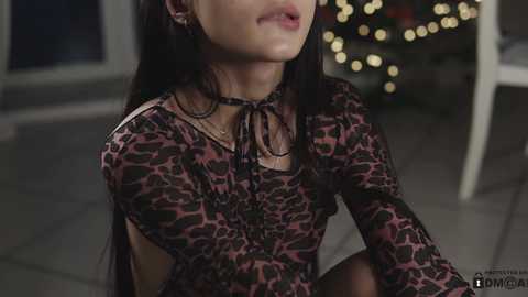 Media: Video of an Asian woman with long black hair, wearing a leopard-print dress, standing indoors with blurred festive lights in the background.