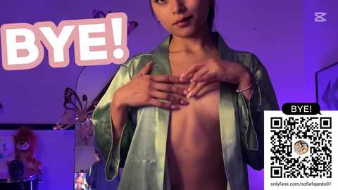 Media: Video of a young woman with light brown skin and short dark hair, partially undressing, revealing her bare chest. Background features a pink \"BIE!\" sign and purple lighting, with a QR code overlay.