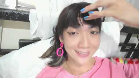 Media: A video of an Asian woman with straight black hair, wearing pink earrings, lying on a bed, being massaged by another hand.