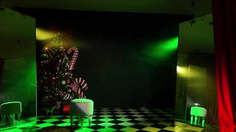 Media: Video of a dimly lit stage with a large, decorated Christmas tree on the left, lit by green and yellow lights, and a checkered black-and-white floor. Two white chairs with red and green cushions are placed in front.