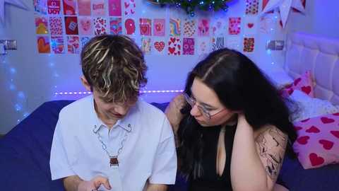 Media: Video of a young boy and a tattooed woman in a cozy bedroom with a heart-decorated wall, blue lights, and a bed with red pillows.