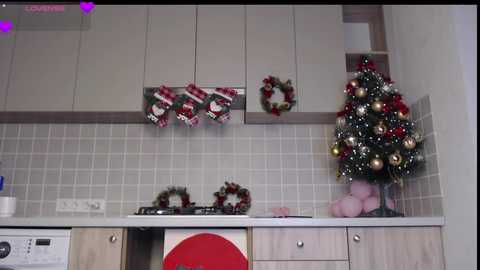 Media: Video of a modern kitchen with beige cabinets, tiled backsplash, a small Christmas tree with ornaments, and hanging stockings.