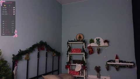 Media: Video of a cozy, blue-walled room decorated for Christmas. White shelves hold red gifts, a green wreath, and a Santa hat. A black ladder leans against the wall, adorned with garlands and ornaments.