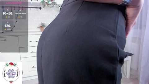 Media: Video of a person in a black skirt, captured from a side angle, showcasing the curves of their buttocks. The background features a white kitchen with cabinets and a potted plant.