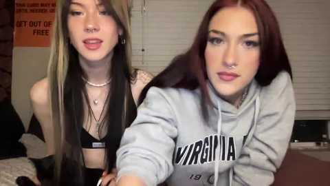 Media: Video of two young women with pale skin and long dark hair, one with a nose ring, wearing a black bra, the other in a grey hoodie.