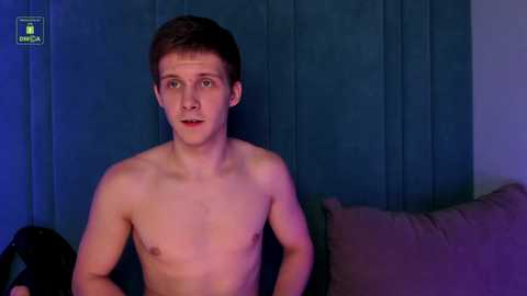 Media: A video of a young, shirtless Caucasian male with fair skin and short brown hair, standing against a dark blue curtain backdrop. He has a neutral expression.