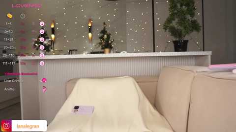 Media: A video of a modern, minimalist room with a white sofa, covered in a beige blanket. The background features a white wall with small, twinkling lights and a potted plant.