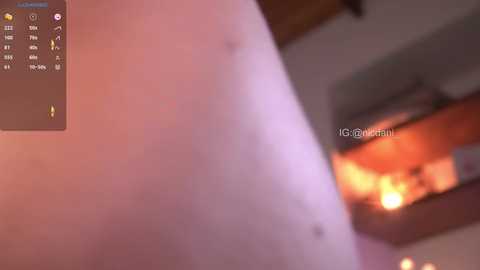 Media: A blurry, close-up photo of a person's arm with a tattoo of a flower, taken indoors with warm lighting. The background shows a wooden ceiling and a fireplace with flames.