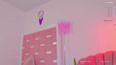 Media: Video of a pink-themed bedroom with a dreamcatcher on the wall, a hexagonal quilted headboard, and a red lamp casting a soft glow.