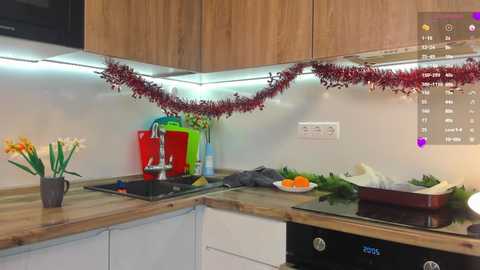 Media: A video of a modern kitchen with wooden cabinets, a black stove, a glass top stove, a red and green garland, a white plate with eggs, and a vase with daffodils.