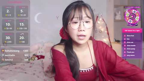 Media: Video of an Asian woman with long black hair in a red dress, wearing glasses, in a cozy bedroom with a bunny-themed bed and a digital thermometer display.