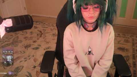 Media: A video of a young person with green hair, glasses, and a white hoodie, sitting on a black gaming chair, in a room with a patterned rug and a white door.