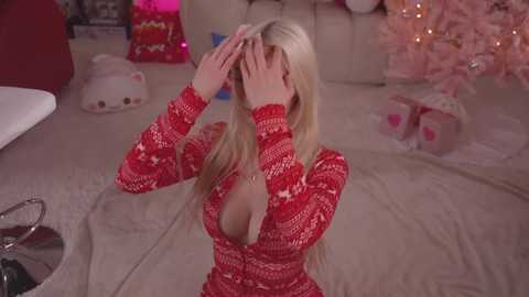 Media: A video of a blonde woman in a red, low-cut sweater, kneeling on a beige carpet, covering her face with her hands, in a festive living room with Christmas decorations.