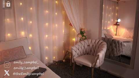 Media: Video of a cozy, romantic bedroom with a plush, white tufted armchair, draped fairy lights, a small side table, and a large mirror reflecting the bed with a soft, white bedspread and a decorative lamp.