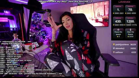 Media: A video of a Twitch streamer with long black hair, wearing a black and red patterned robe, sitting on a gaming chair, with a monitor displaying chat messages and viewers' names.