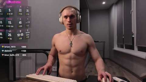 Media: Video of a shirtless, muscular, young man with fair skin, wearing headphones, seated at a desk in a dimly lit room, with a digital display showing streaming stats.