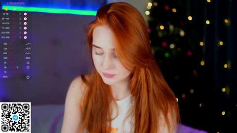 Media: A video of a fair-skinned, red-haired woman with long, flowing locks, wearing a white shirt, standing indoors next to a Christmas tree with glowing lights. The background shows a digital interface with a green bar and a QR code.