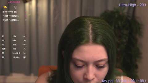 Video of a young woman with straight, dark green hair, eyes closed, and a serene expression, captured by UltraHigh 2018. Background shows dimly lit curtains and a soft focus.