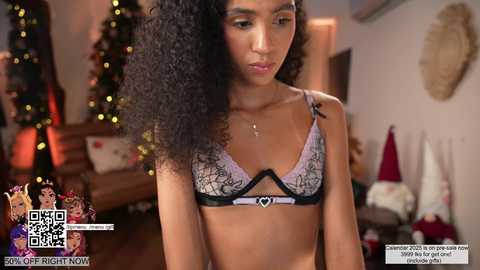 Media: Video of a young Black woman with curly hair, wearing a lavender bra with black lace, in a cozy, festive room with a Christmas tree and wreaths.