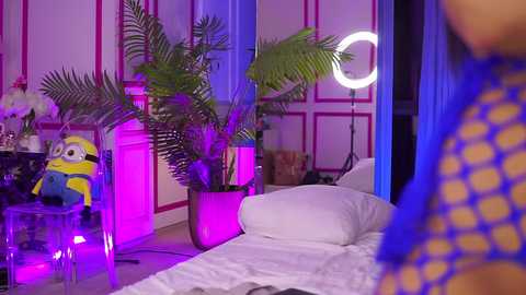 Media: Video of a colorful, modern bedroom with vibrant purple and blue lighting, a large potted plant, a Minnie Mouse plush, a fish tank, and a circular mirror.