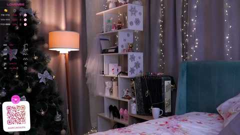 Media: Video of a cozy bedroom with a lit Christmas tree, a tall floor lamp, a white bookshelf filled with decorations, and a teal upholstered headboard.