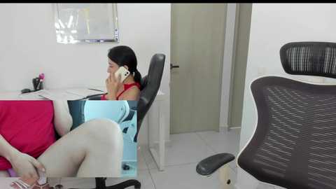 Media: A video of a modern office with a woman in a red top and black leggings on a chair, talking on a phone, next to a white desk with a pink mug.