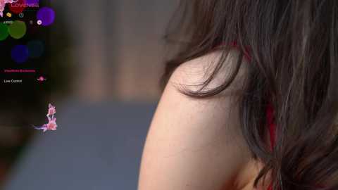 Media: Video of a woman with shoulder-length brown hair and a red bra strap, viewed from the side. A pink, animated character, resembling a cat, is in the foreground. Background is blurred.