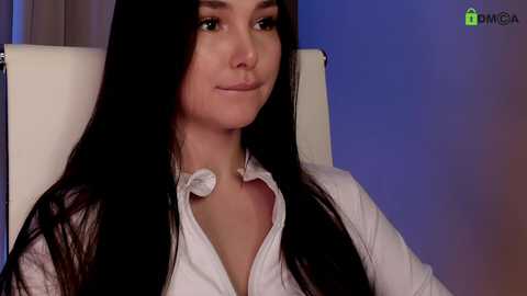 A video of a woman with long black hair, fair skin, and dark eyes, wearing a white shirt with a collar unbuttoned, sitting in a white chair against a blue and purple background.