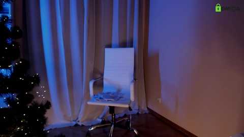 Media: Video of a modern white office chair against a dimly lit, beige wall with soft blue lighting. A decorated Christmas tree with twinkling lights is partially visible on the left.