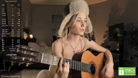 Media: Video of a topless woman with a large fur hat playing an acoustic guitar in a dimly-lit living room.