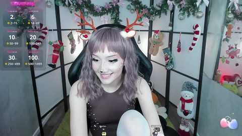 Media: Video of a young woman with light skin and wavy gray hair, wearing a black sleeveless top and red antlers, sitting in a festive room with holiday decorations.