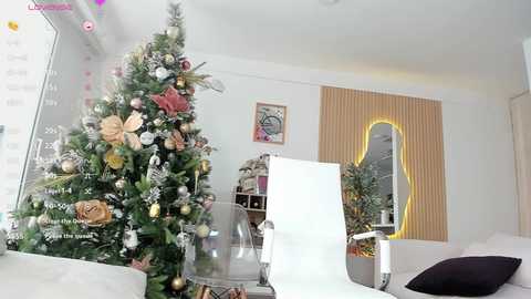 Media: Video of a modern, well-decorated living room with a white armchair, a clear acrylic chair, a tall Christmas tree adorned with gold and silver ornaments, and a mirrored wall with a large, yellow-framed mirror.