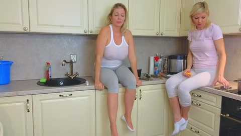 Media: Video of two women in casual attire, one in a white tank top and gray leggings, the other in a white t-shirt and leggings, sitting on kitchen counters.