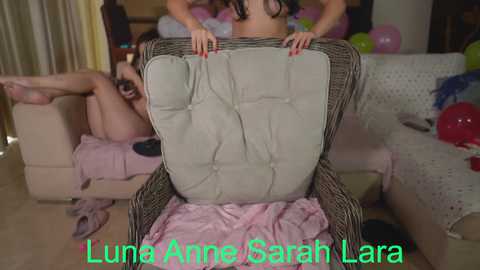 Media: Video of a young woman, Sarah Lara, in a cozy living room, sitting on a beige couch with a white cushion. She wears a pink top, red nail polish, and a pink blanket.