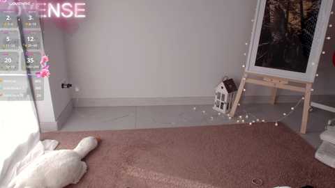 Media: Video of a cozy room with a white cat, a pink plush toy, and a wooden easel with a white frame, illuminated by fairy lights.