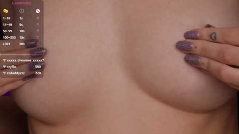 Media: A close-up video of a woman's bare chest, featuring large, round, natural breasts. She has a fair complexion and is cupping her breasts with both hands, adorned with glittery purple nail polish. The background is blurred.