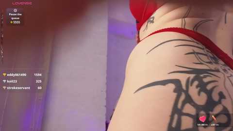 Media: Video of a person's backside in red lingerie, featuring a large, intricate black tribal tattoo on the right hip. The background is blurred, with a social media interface visible on the left.