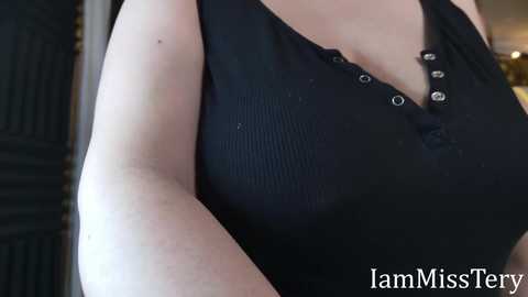 Media: Video of a light-skinned person wearing a black ribbed tank top with small buttons, emphasizing a curvy chest. Background includes a dark, possibly wooden door. Text \"IamMissFerry\" in white at bottom right.