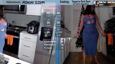 Media: Video of a woman in a blue dress, standing in a modern kitchen with appliances and a Christmas tree.