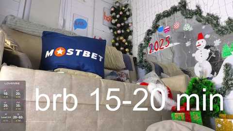 Media: Video of a festive living room with a cozy sofa, decorated with a \"MOSTBET\" pillow, a Christmas tree, a snowman ornament, and holiday gifts, with a 15-20 minute timer overlay.