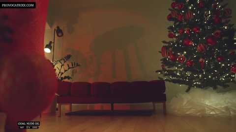 Media: A video of a cozy, dimly lit room with a red velvet couch, a Christmas tree adorned with red ornaments, and a red curtain on the left. A warm, ambient light casts a soft glow.