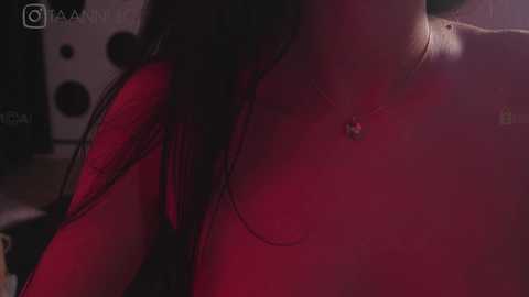 Media: Video of a close-up of a woman's neck, wearing a red top and a silver necklace, dimly lit, blurred background, suggestive lighting.