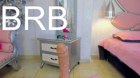 Media: Video of a pink-themed bedroom with a large, erect penis in the foreground, a vanity table with makeup, and a bed with pink bedding.